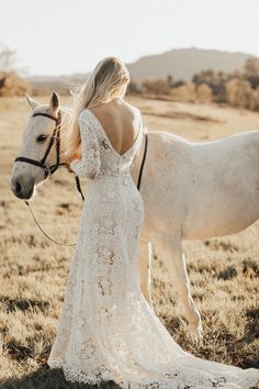 a beautiful blonde woman in a white dress standing next to a horse on a field