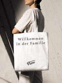 a woman carrying a white shopping bag that says willkommen in der familie