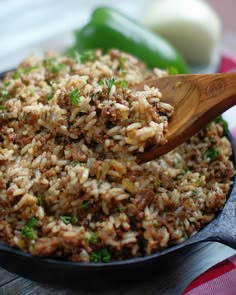 a skillet filled with rice and meat on top of a wooden table next to green peppers