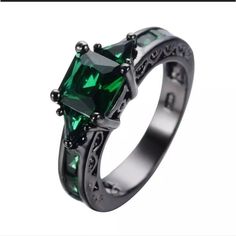 an emerald colored ring with black diamonds on the sides and green stones in the middle