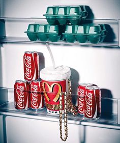 a refrigerator filled with lots of coca - cola cans next to bowls and trays