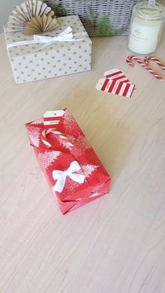 two wrapped presents sitting on top of a wooden table next to candles and candy canes