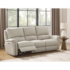 a white leather reclining sofa sitting on top of a wooden floor next to a window