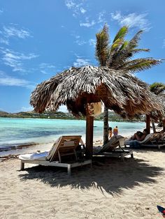 some people are laying on lounge chairs under a straw umbrella and palm trees at the beach