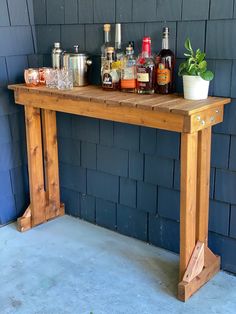 a wooden table topped with lots of bottles and glasses next to a blue brick wall