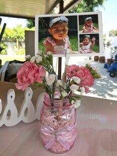 a pink mason jar with flowers in it sitting on a table next to a photo frame