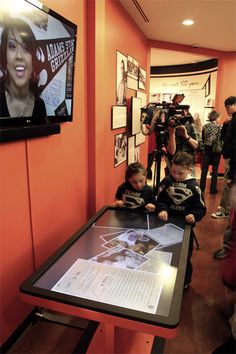 two young boys sitting at a table in front of a screen with pictures on it