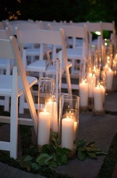 rows of white chairs with lit candles on the ground in front of them at an outdoor ceremony