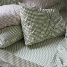 pillows are stacked on top of each other in front of a bed with green and white checkered sheets