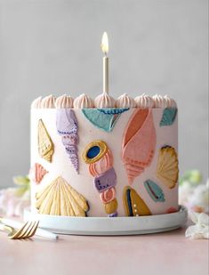 a birthday cake with seashells on it and a single candle in the middle