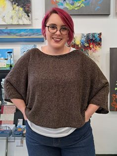 a woman with pink hair and glasses standing in front of paintings