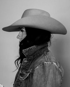 a woman wearing a cowboy hat and denim jacket looking off into the distance with long hair