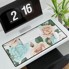 a computer desk with a clock and flowers on the mouse pad, next to a plant