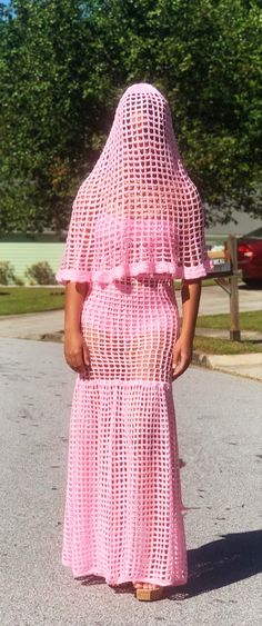 a woman in a pink crochet dress is walking down the street with her back to the camera