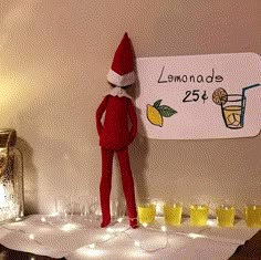 an elf is standing next to a sign with lemonade on it and glasses in front of him