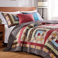 a bed with a colorful quilt on top of it next to a night stand and lamp