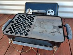 a grill with two controls on top of it sitting on a wooden deck next to a wall