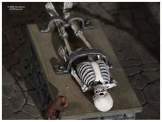 a skeleton laying on top of a cement block next to a small toy squirrel sitting in front of it