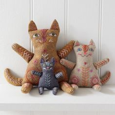 three handmade cats sitting on top of a shelf next to each other, with one cat's eyes open