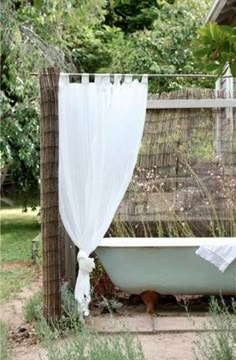 an old bathtub with sheer curtains in the yard