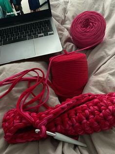 a laptop computer sitting on top of a bed next to red yarn