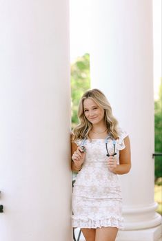 a beautiful young blond woman standing next to a white column holding some blue scissors in her hands