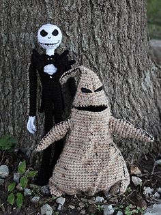 two crocheted dolls standing next to a tree