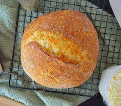 a loaf of bread sitting on top of a cooling rack next to some cheeses