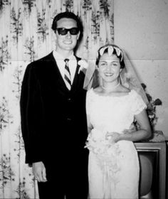 a man and woman in wedding attire standing next to each other with sunglasses on their faces