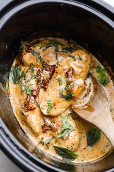 a wooden spoon in a crock pot filled with chicken and spinach curry sauce