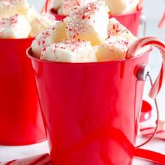 two red mugs filled with marshmallows and candy canes on a white table