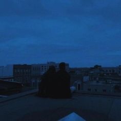 two people sitting on top of a roof at night