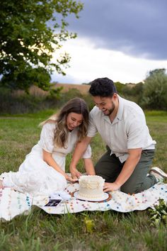 a man and woman cutting a cake on a blanket in the middle of a field