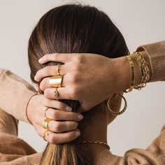 a woman with her hair in a ponytail wearing gold rings and bracelets, holding her hands on the top of her head