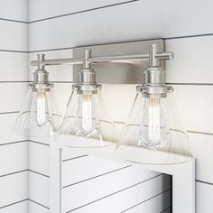 three light bathroom fixture with clear glass shades on the mirror and white paneled wall