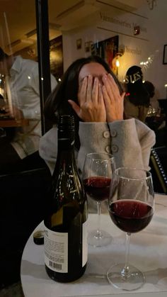 a woman covering her face next to two glasses of wine