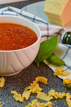 a bowl of tomato soup with basil leaves on the side