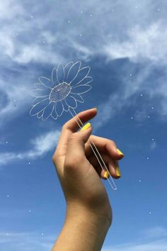 a hand holding a string with a flower on it in front of a blue sky