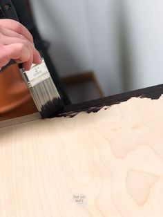 a person using a brush to paint a piece of wood with black paint on it