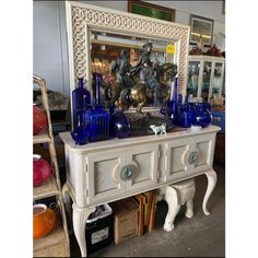 a white dresser with blue glass vases and a mirror on it's side