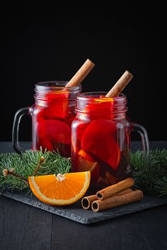 two mason jars filled with apple cider next to cinnamon sticks and orange slices on a slate board