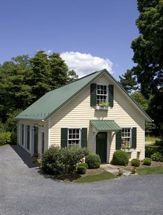 a small white house with green shutters on the front and side windows, surrounded by trees