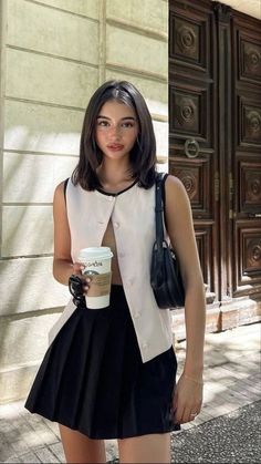 a woman holding a cup of coffee standing in front of a building