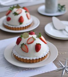 two small cakes with white frosting and strawberries on top, sitting on plates