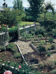 a garden with lots of plants and rocks in it's center, next to a white picket fence