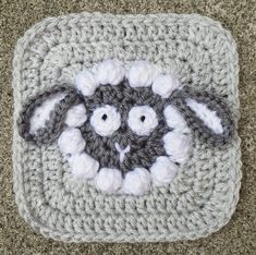 a crocheted square with an animal face on the center and two white eyes