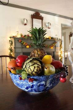 a blue and white bowl filled with fruit on top of a wooden table next to a fireplace