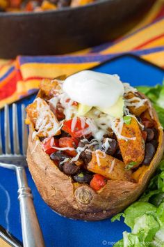 a blue plate topped with a baked potato covered in black beans, cheese and lettuce