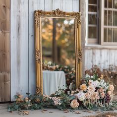 a mirror sitting on top of a wooden floor next to flowers and greenery in front of a building