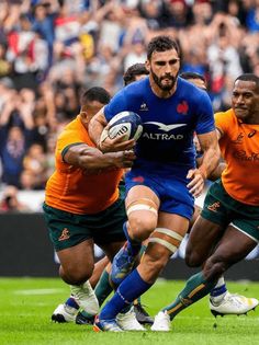 the rugby players are running with the ball in their hands as an audience looks on